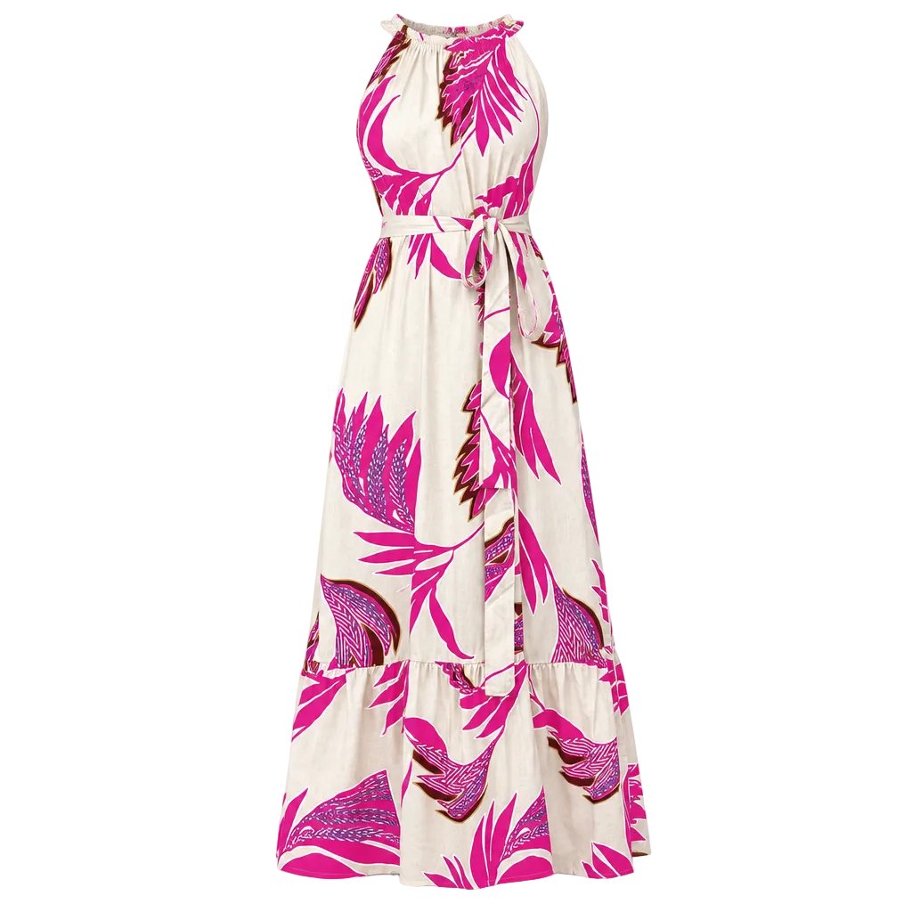 A woman wearing a sleeveless, high-neck, floor-length maxi dress with a bold pink and purple tropical leaf print on a cream background, standing indoors against a light-colored wall.