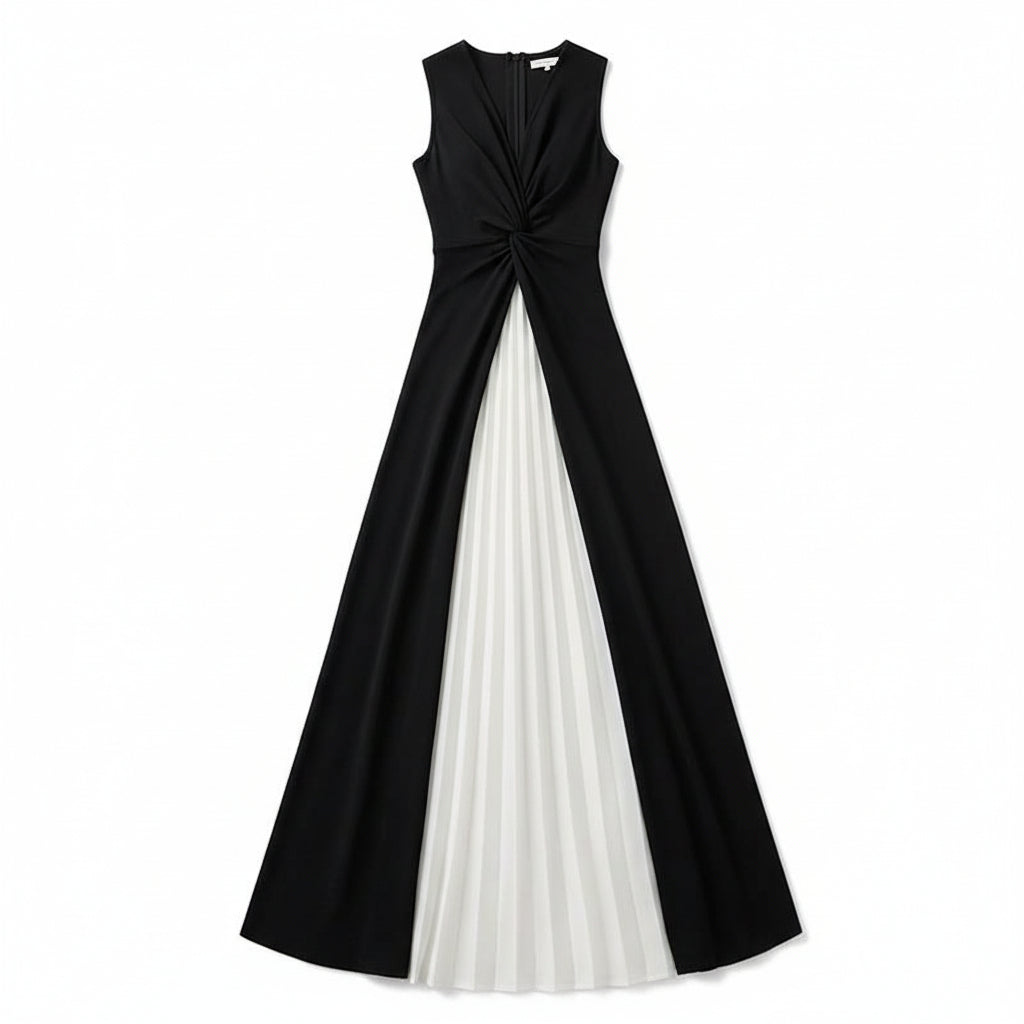 A woman wearing a sleeveless black and white color-block maxi dress with a twisted front detail, holding a woven straw handbag with a black leather pocket and gold chain strap, standing outdoors on a paved walkway.