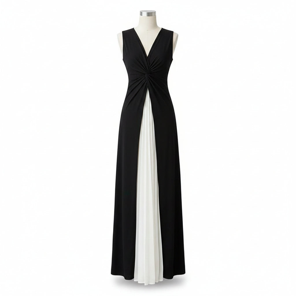 A woman models a sleeveless black and white maxi dress with a twisted bodice, holding a woven straw handbag in an outdoor urban setting.